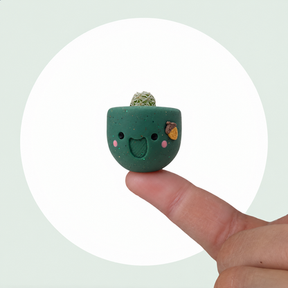 Acorny live mini cactus in a handmade sage green pot with rosy cheeks and a tiny acorn, balanced on a fingertip