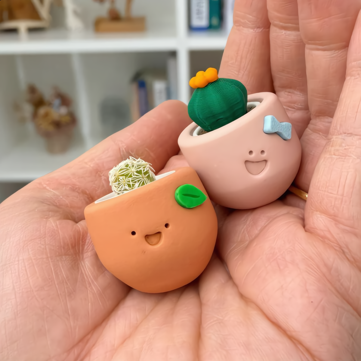 Two smiling tiny cactus pots held in the palm of a hand